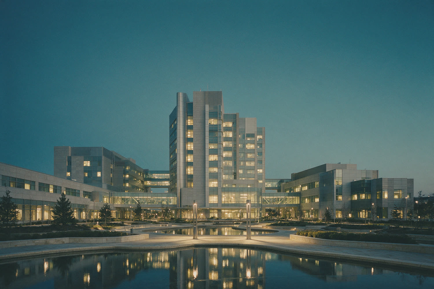 A large hospital campus of connected buildings at dusk, windows lit